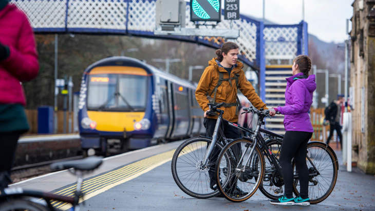 Two people standing with folding bikes at a train station