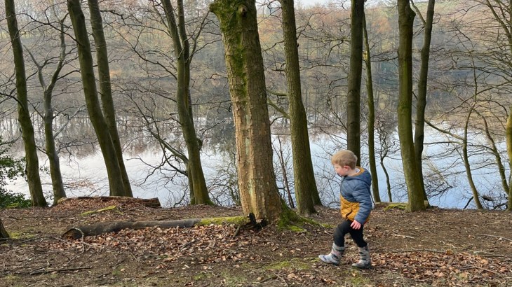 Little boy side on walking through woodlands with his wellies on 