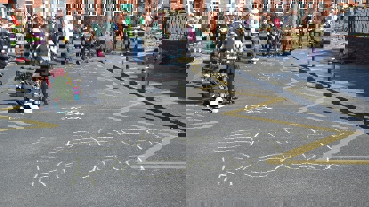 road outside school is closed to cars and children are playing and drawing with chalk