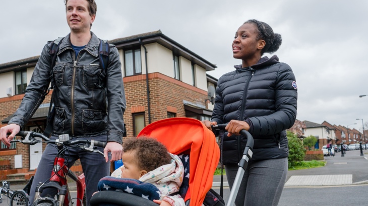 A man with a bike and a woman pushing pram chatting in a quiet residential area