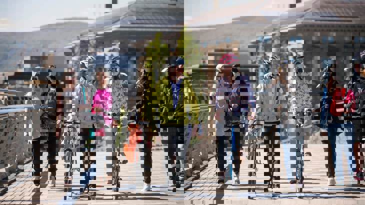 People walking and on bikes crossing bridge in urban setting