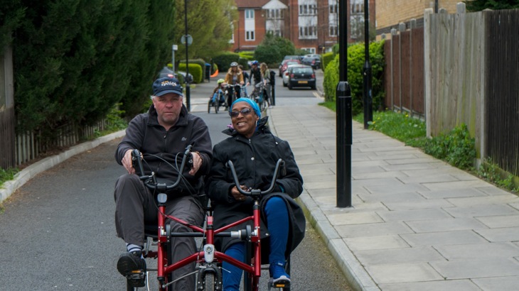 Two people smiling as they ride a recumbent adapted cycle along London Quietway 1 route