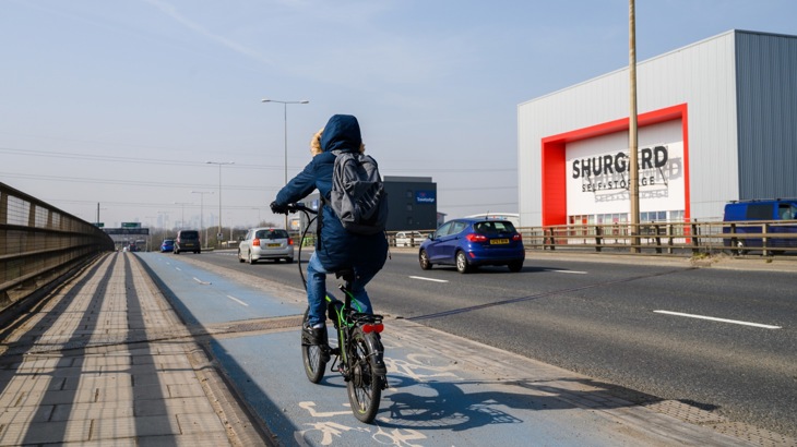 Cyclist in a coat on a segregated cycle lane on a busy dual carriageway