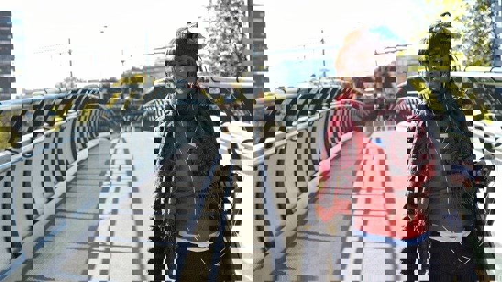 Woman in coat and scarf with earphones on walking across bridge