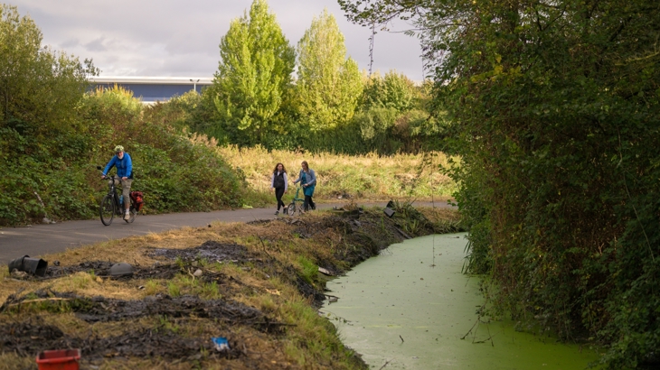 walking and cycling a route that lines as waterway. The water is green with algae and the banks littered on. and 
