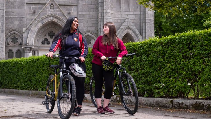 Two teenage girls laughing as they stand and talk next to their bikes