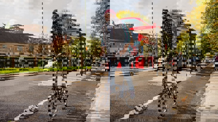 Man in hat and scarf riding fold-up bike in city cycle lane with red double-decker bus in background