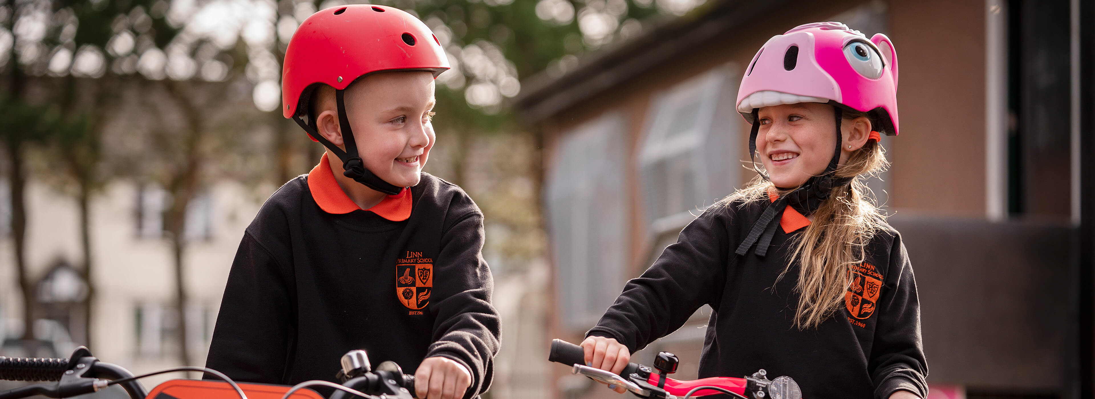 Two children walking next to their bikes smiling at each other