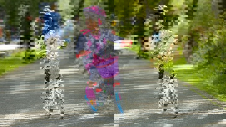 Toddler riding a pink bike on a path through a park 