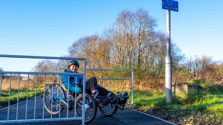 Cyclist on recumbent trike navigating accessible barriers.