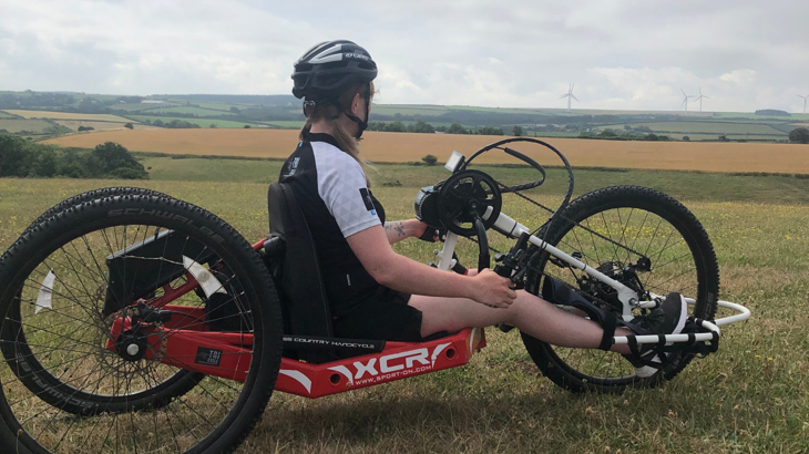 Laura sat on her red XCR handcycle, looking over rolling countryside with wind turbines on the horizon.