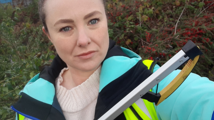 An image of Walk Wheel Cycle Trust volunteer, Lauren, whilst she's out on a litter pick. The image shows Lauren, in a high-vis tabard, in front of some greenery, holding a litter picker and looking into the camera.
