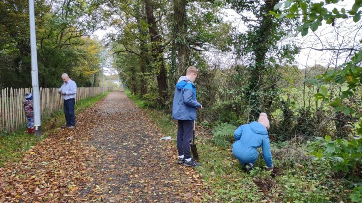 A man, a woman, a teenage boy and young girls are collecting litter along a secluded path.