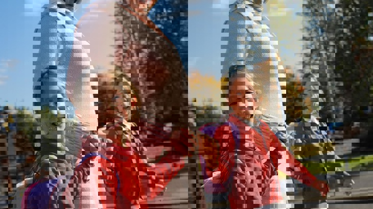 Mum walking to school, holding hands with her twin daughters smiling at the camera