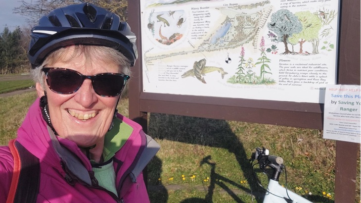 Karen is shown standing in front of an information board at a nature reserve.