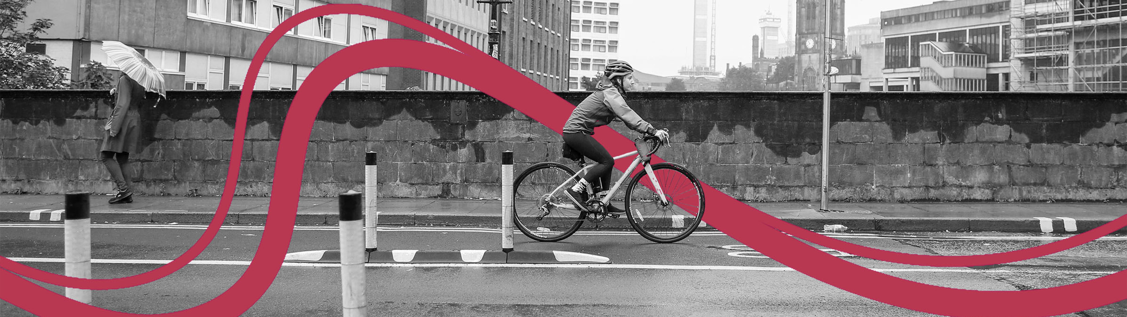 Person cycling on a temporary segregated cycle route along a road, wearing a waterproof jacket and a helmet. Photo is in black and white.