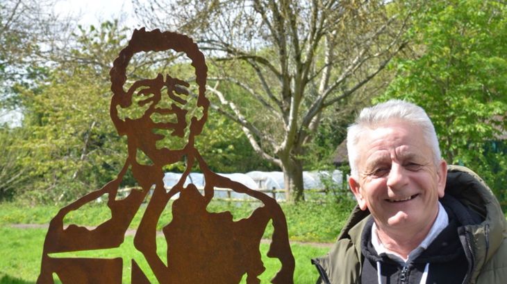 Local community volunteer stands next to the portrait bench of him on the national cycle network in Lawrence Weston, Bristol.