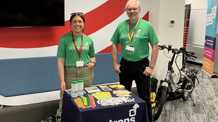 Two Walk Wheel Cycle Trust colleagues standing at an information stall with an Ecargo bike next to the table.
