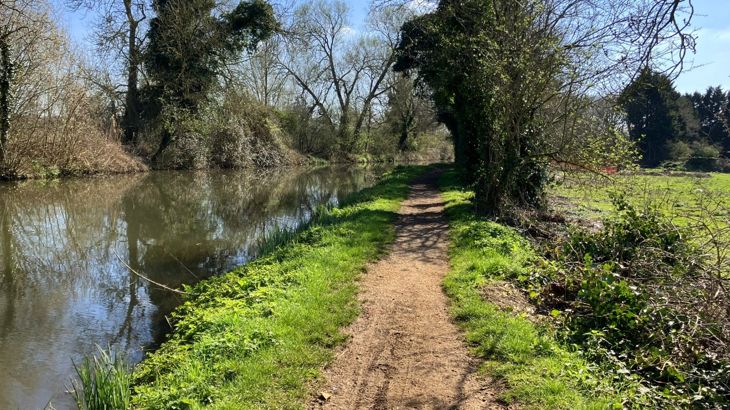 Canal towpath before works. Narrow mud path, lined with grass, next to a canal.