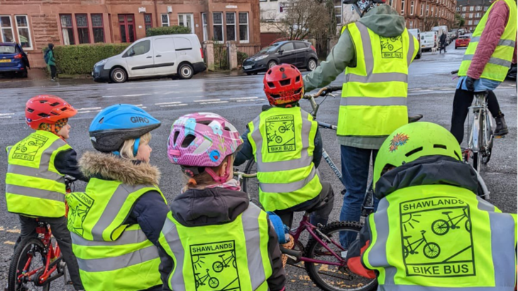 A group of children and adults on bikes stopped at a crossing whilst on their bike bus to school.