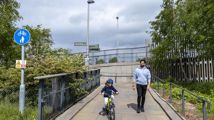 A child is pictured cycling down a ramp on a cycle path in Inverness. They are accompanied by an adult who is walking next to them.