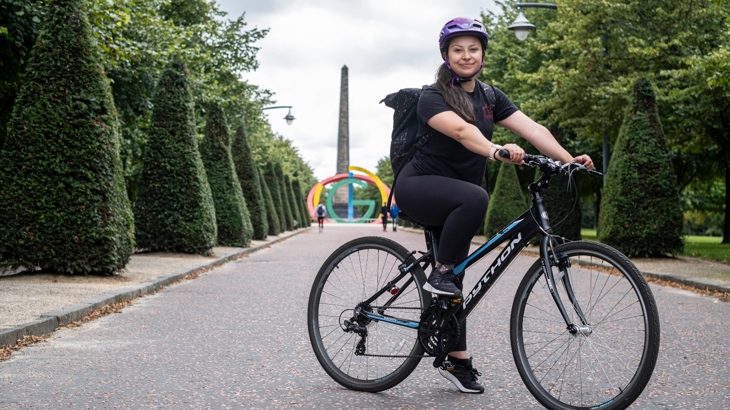 A woman sits on her bike and smiles to camera on a traffic-free path lined by topiary hedges in the centre of Glasgow.