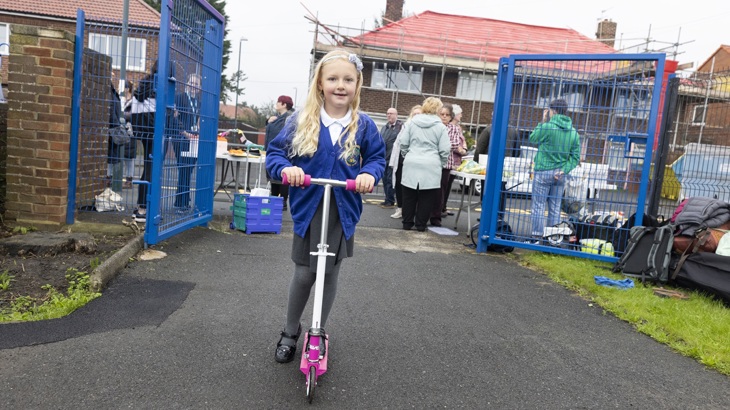 young girl on a scooter coming through the school gate