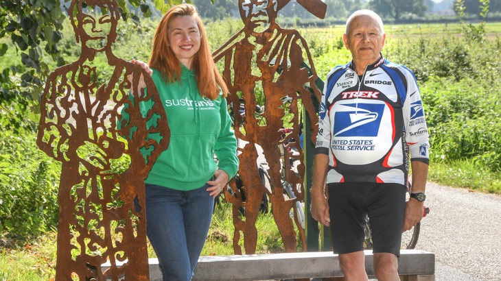 a woman and a man stand next to life-sized metal sculptures of the actor Dame Judi Dench, and cycle route builder Dave Jackson