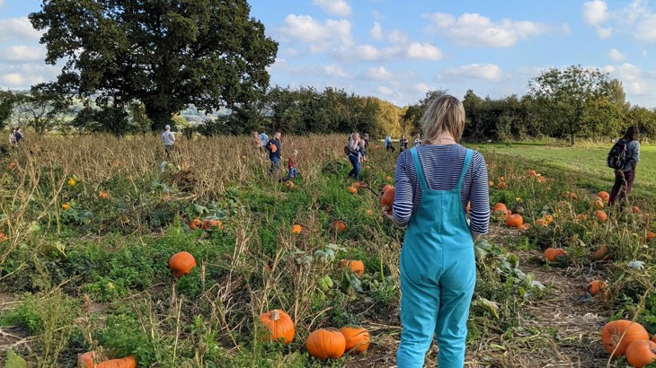 Woman and family standing in pumpkin patch field with blue skies.