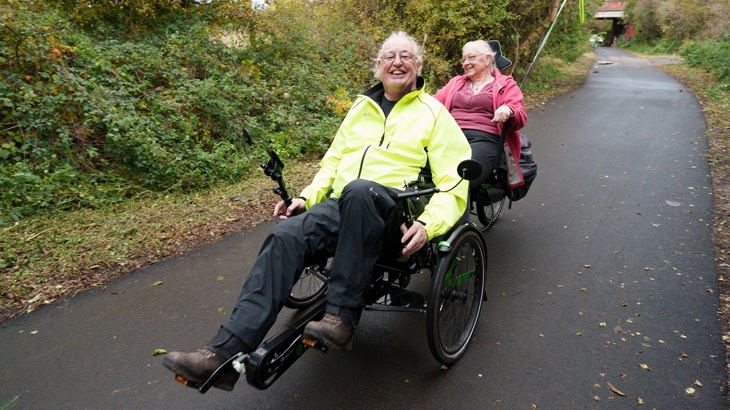 two people riding on an adapted cycle and smiling