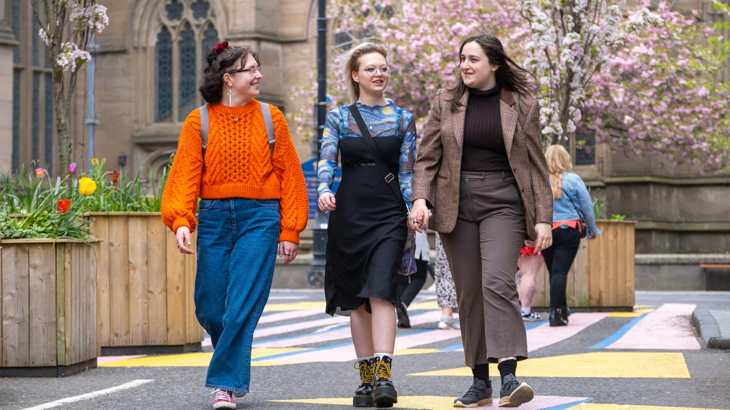 Three people cross a road that has been blocked off to traffic