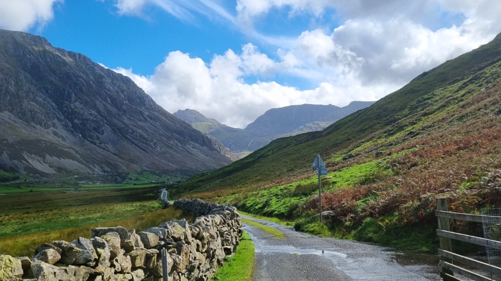 Country-lane winding through a valley, surrounded by steep hills and mountains.
