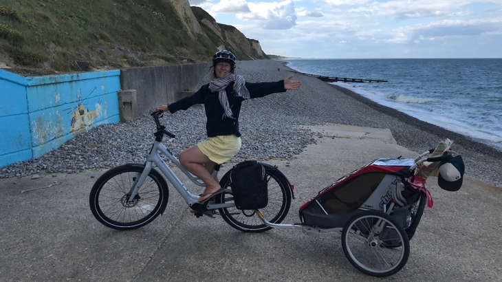 Nia on her e-bike with an attachment on the back, on the coastline.