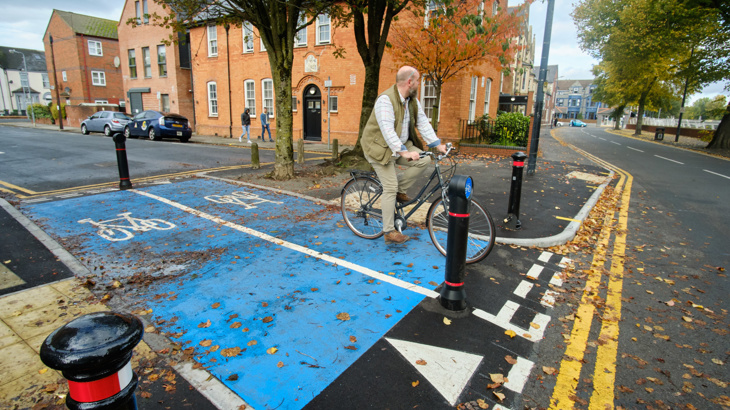 A cyclist approaches a junction leading onto a road in a residential area.