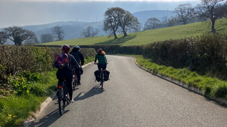 Three cyclists on a rural NCN route, with green hills around them.