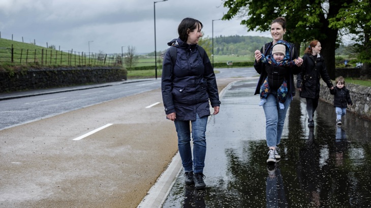 A group of people are shown walking on a pavement in the rain.