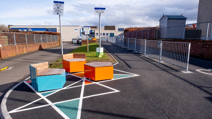 A parent/carer and school pupil walk past planters in the grounds of their primary school.