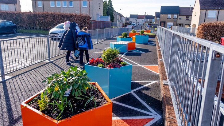 A parent/carer and school pupil walk past planters in the grounds of their primary school.