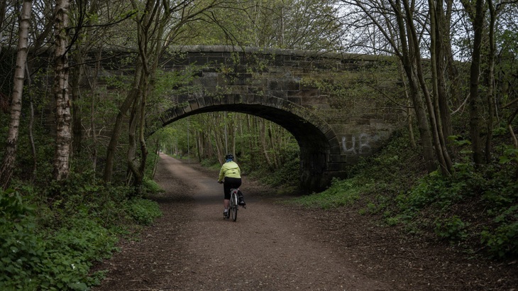 A person is shown cycling under a bridge on a traffic-free path in wooded land in Dunfermline.