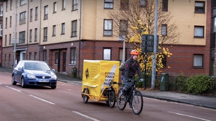 The Glasgow Tool Library e-bike trailer is shown being cycled in the city.