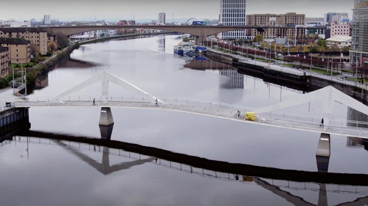 The Glasgow Tool Library e-bike trailer is shown being cycled across a bridge in the city.