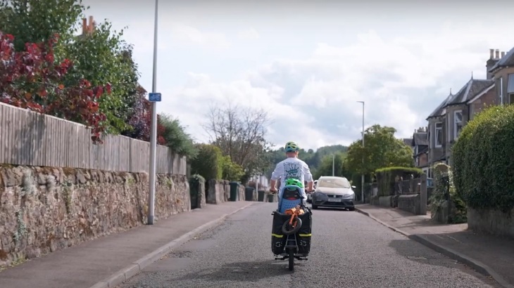 Robin is pictured riding an e-cargo bike with his children on a residential street