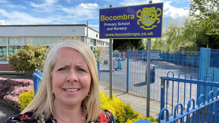 A woman with blonde hair stood smiling outside of the primary school where she teaches on a sunny day in spring