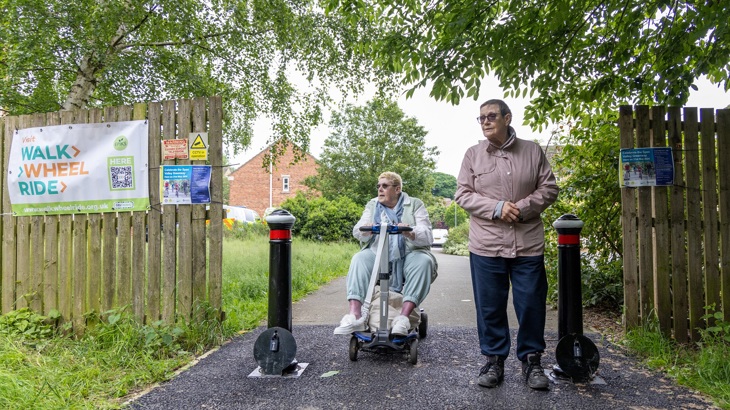 a woman on a mobility scooter and a man walking next to her on a walking, wheeling, cycling route
