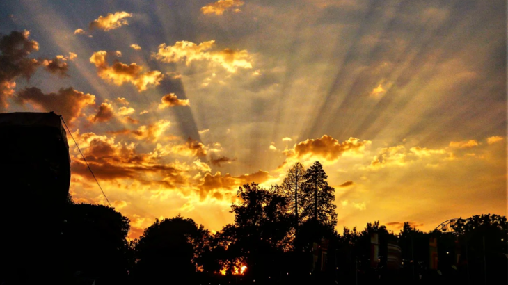 The sun setting behind some buildings, causing the clouds to glow golden.