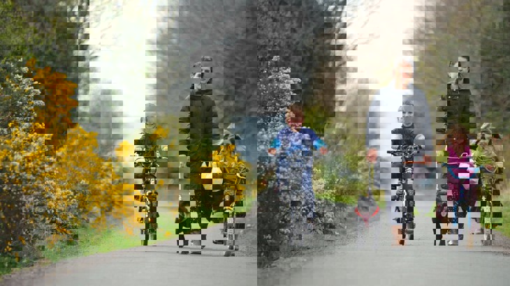 Young boy and girl cycling on cycle path with woman walking a dog