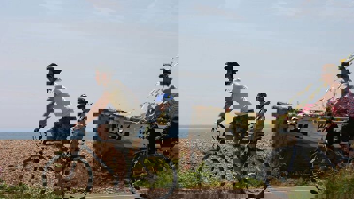 Cyclist with young child in bike seat with woman cyclist behind on coastal route