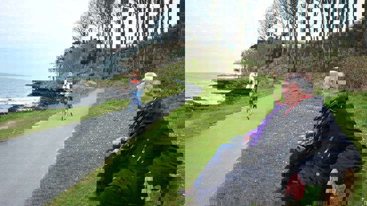 Couple sitting on park bench, looking at cyclist on coastal cycle path