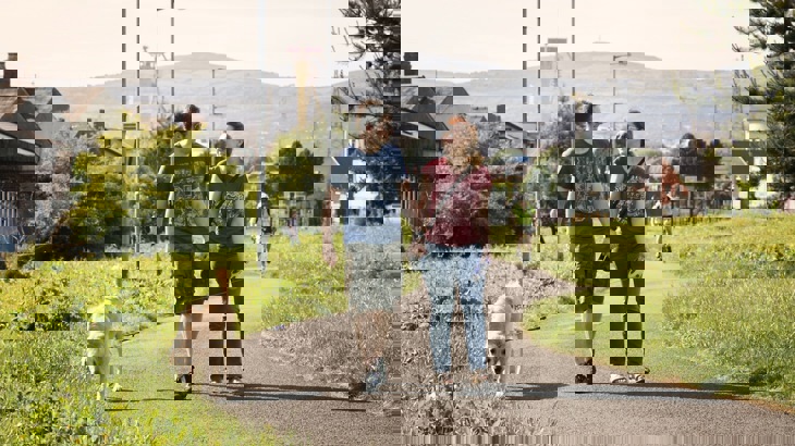 Man and woman holding hands and walking dog on path in suburban area