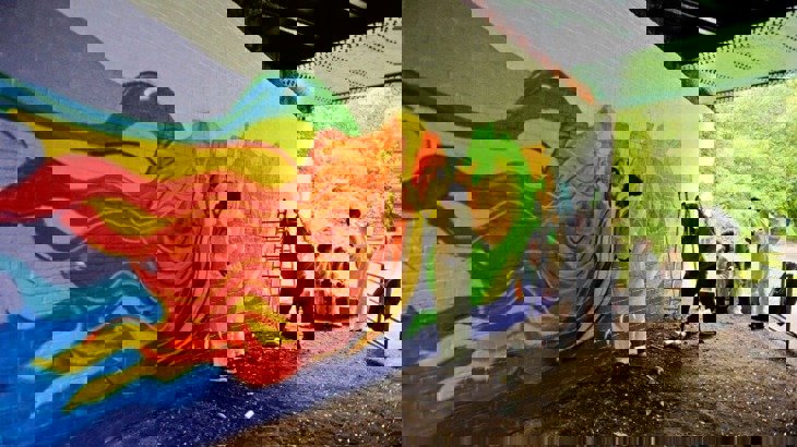 Teenagers painting a dragon mural under a bridge